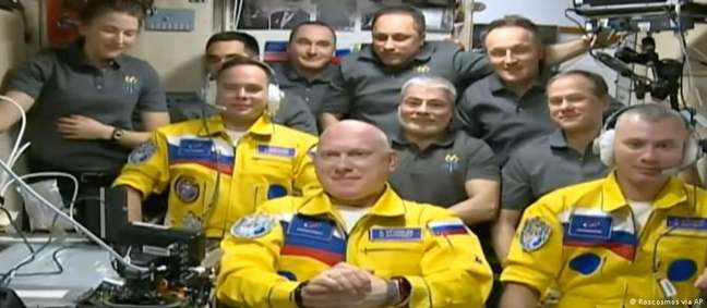 Cosmonautas russos em trajes com cores ucranianas são recebidos por colegas na ISS