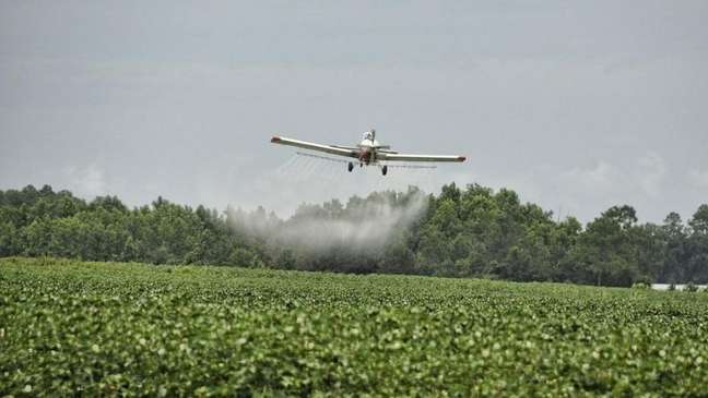 Foto de um avião despejando agrotóxico sobre uma plantação.