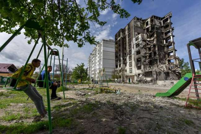 Dois jovens conversando bem próximos de um edifício destruído em Borodyanka