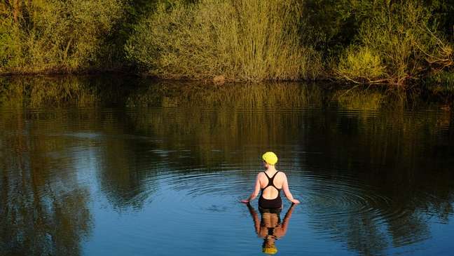 Mulher entrando em um rio de maiô e touca de natação