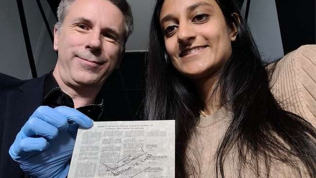 Spencer e Dhara posam para uma selfie com um documento legal que foi enviado à Lua