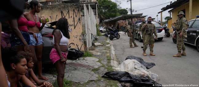 Moradores e policiais ao lado de um corpo coberto após operação policial que deixou 23 mortos na Vila Cruzeiro, Rio de Janeiro
