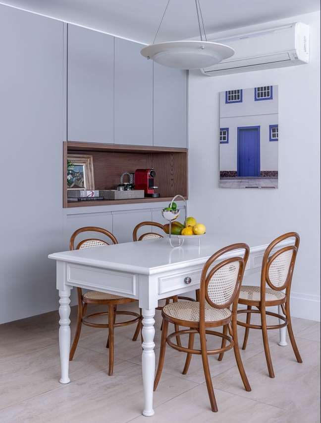 Cozinha com armários azuis, quatro na parede lateral, mesa branca com quatro cadeiras ao seu redor.