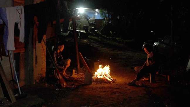 Seu Nenê sentado ao lado de fogueira com o filho em noite fria no distrito de Marsilac