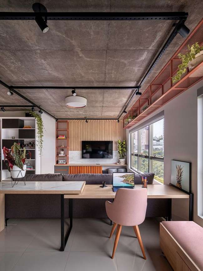 Foto mostra mesa de home office e cadeira rosa em sala de estar de estilo industrial.
