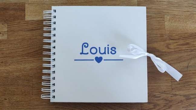 Um álbum de fotos em espiral branco com o nome Louis escrito em azul