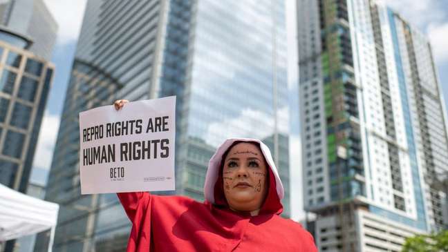 Direitos reprodutivos são direitos humanos, diz cartaz de manifestante a favor do direito de abortar vestida como personagem de " O Conto da Aia"