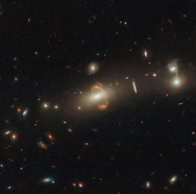 A galáxia duplicada pela lente gravitacional, no centro da imagem, também está espelhada (Imagem: Reprodução/ESA/Hubble/NASA/J. Rigby)