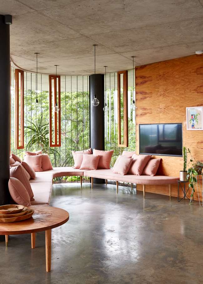 Living room and TV with pink sofa and glass sheets that allow a view of the woods.