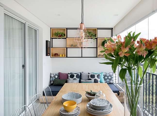 In this project by doob Arquitetura, the dining table shares balcony space with a futon-style sofa and a charming structure that houses potted plants. In this project by doob Arquitetura, the dining table shares balcony space with a futon-style sofa and a charming structure that houses potted plants.