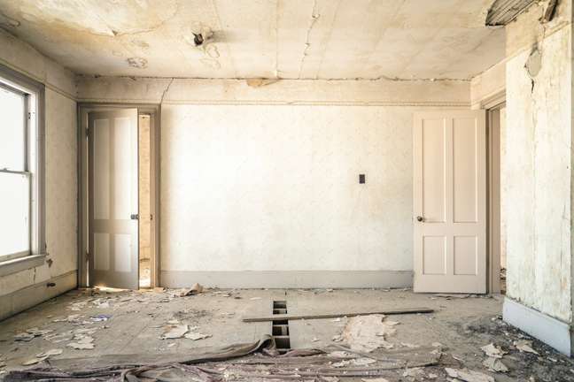 Foto mostra sala de casa com piso destruído, paredes e teto com danos.