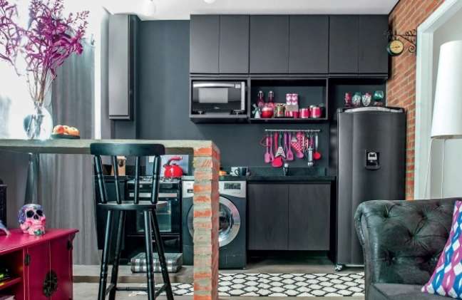 The photo shows the kitchen with cabinets covered in matte black laminate, dining bench with concrete top and exposed brick structure.
