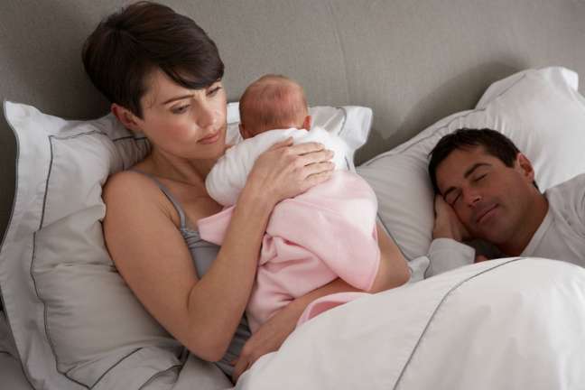 couple lying in bed. Cute woman holds a baby while the man sleeps couple lying in bed. Cute woman holds a baby while the man sleeps