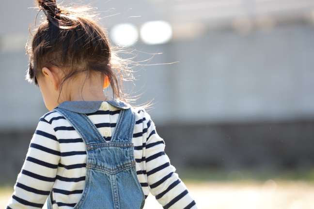 small boy from the back, with brown hair tied back, wearing a striped shirt and denim overalls small boy from the back, with brown hair tied back, wearing a striped shirt and denim overalls