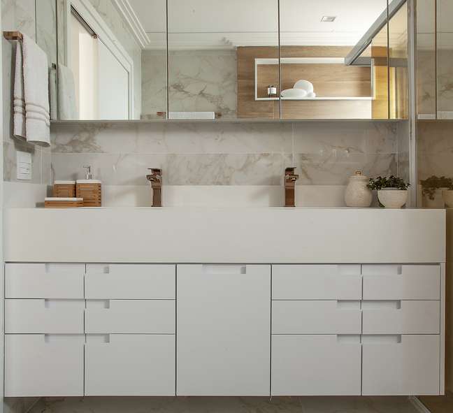 In this elegant bathroom, the white countertop, marble-emulating porcelain tile covers the walls and floor, and gold-plated faucet features a plug next to the switch so the resident can use the electronics in the bathroom, such as hair dryers and irons.