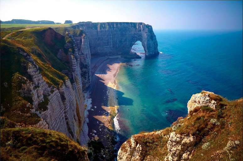 Etretat, França: situado na região da Normandia, no norte do litoral atlântico da França, o vilarejo de Etretat é conhecido por seus imponentes penhascos que se encontram com o oceano.  A 40 metros da praia da cidade, os penhascos brancos cobertos de vegetação têm o auge beleza em seus arcos brancos