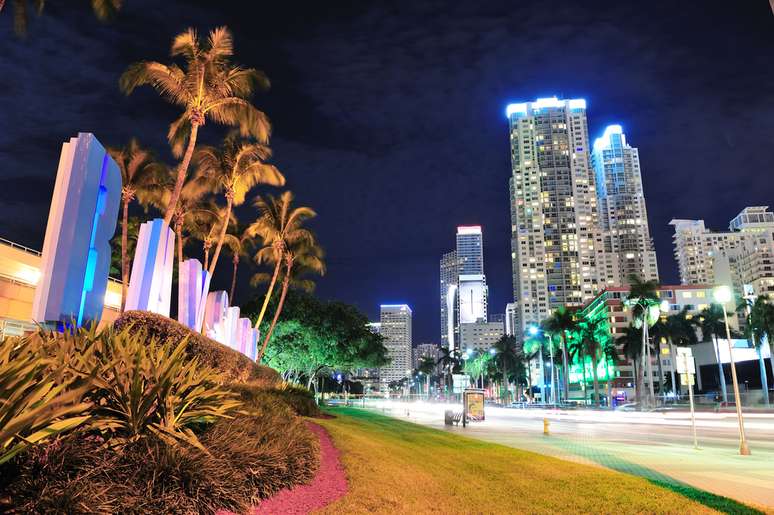 Vista da cidade em frente ao Bayside Marketplace, no centro de Miami. À noite, a região e os bairros próximos viram palcos de um verdadeiro show de luzes. Enquanto o Miami Tower, edifício comercial símbolo da cidade, ganha novas cores sem aviso prévio, hotéis e restaurantes embelezam as ruas com fachadas luminosas. Até mesmo a antiga Miami Bridge, construída em 1939, ganha um novo charme após o crepúsculo. Se de dia a cidade é abençoada pelo Sol, à noite Miami brilha em tons que se perdem ladeira abaixo.