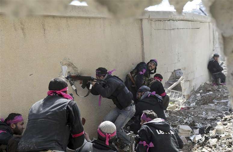 <p>Combatente do Exército Sírio Livre dispara rifle por um buraco na parede de uma base militar síria durante confronto no bairro de Arabeen, em Damasco</p>