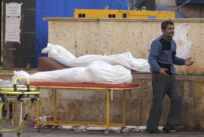 Homem passa perto de dois corpos, em frente a um hospital em Aleppo, na Síria. Pelo menos 100 soldados sírios e 30 rebeldes da milícia Frente Al Nusra, ligada à Al Qaeda, morreram em três dias de combates em uma cidade perto da fronteira iraquiana tomada pelos insurgentes na quinta-feira, informou um grupo de oposição que monitora o conflito sírio. 13/02/2013