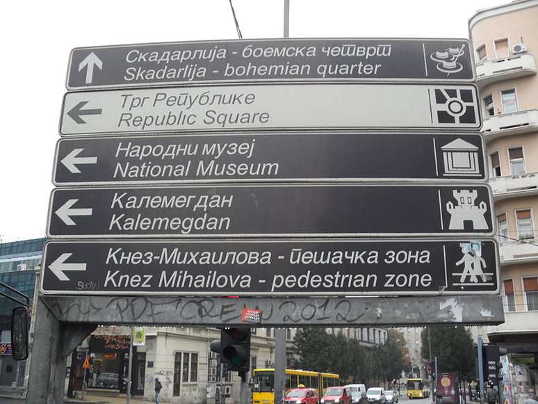 Placa em Belgrado (Sérvia) em alfabeto cirílico e tradução ao inglês; para criador de alfabeto fonético, mal-entendidos linguísticos distanciam as pessoas