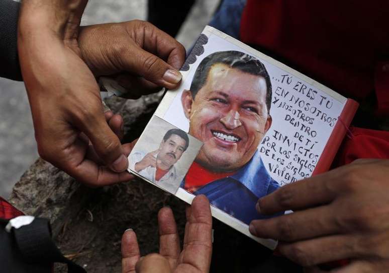 Partidário do presidente da Venezuela Hugo Chávez cola uma foto do presidente atuante Nicolás Maduro sobre uma foto de Chávez em Caracas, Venezuela. 11/03/2013