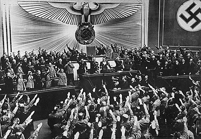 <p>Adolf Hitler é aplaudido pelo Parlamento alemão em março de 1938 após a anexação da Áustria</p>