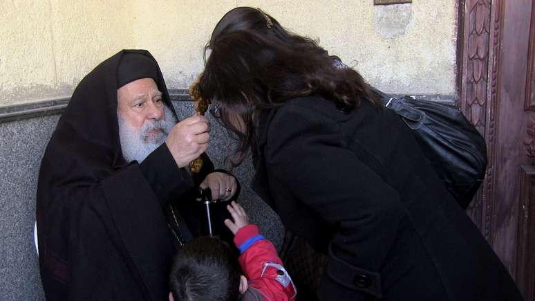  O padre Makary Yunan (esq.) reza por uma família de cristãos na catedral antiga do Cairo