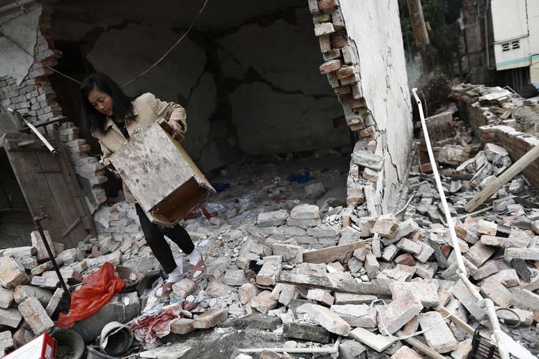Moradora de Lingguan, na província de Sichuan, carrega móvel de sua casa destruída pelo terremoto
