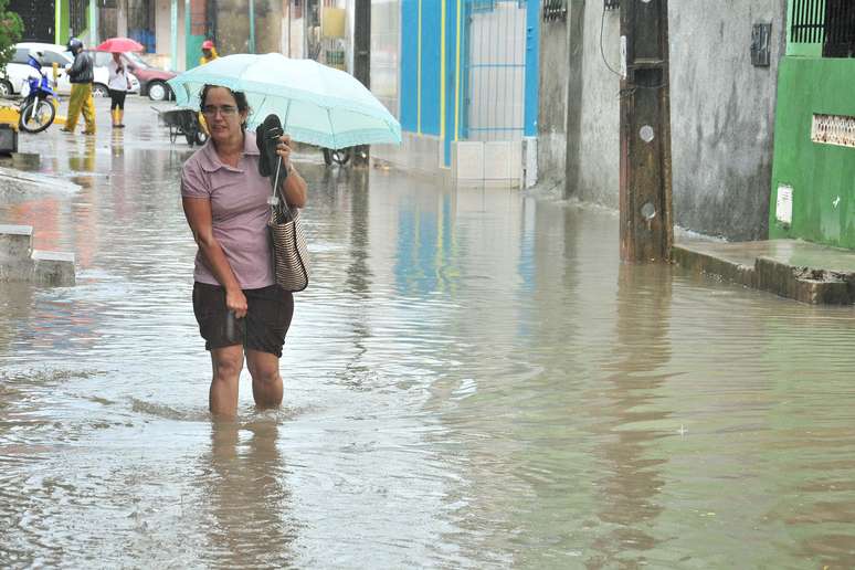 Mulher tira os sapatos para caminhar por rua alagada devido à forte chuva em Salvador