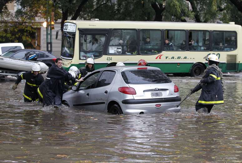 Nas ruas de Buenos Aires, bombeiros tentam evitar que carro seja levado pela força da água
