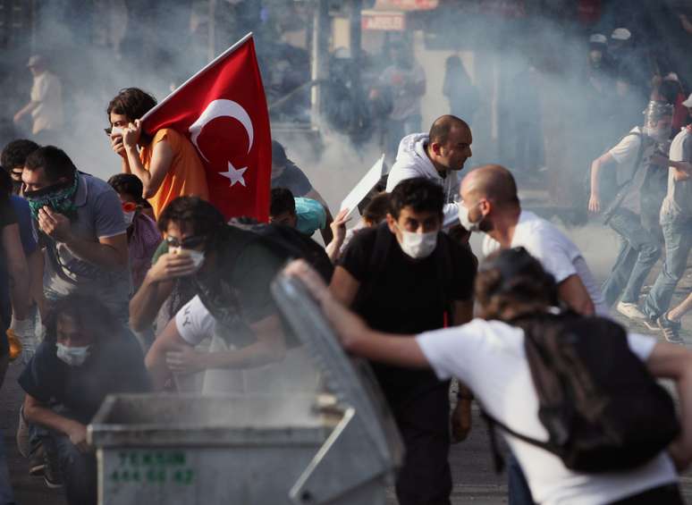 <p>Manifestantes se protegem de bombas de gás lacrimogêneo jogadas pela polícia em Ancara</p>