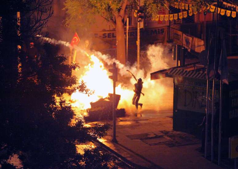 Manifestante joga de volta uma bomba de gás lacrimogêneo arremessada por policiais em Ancara