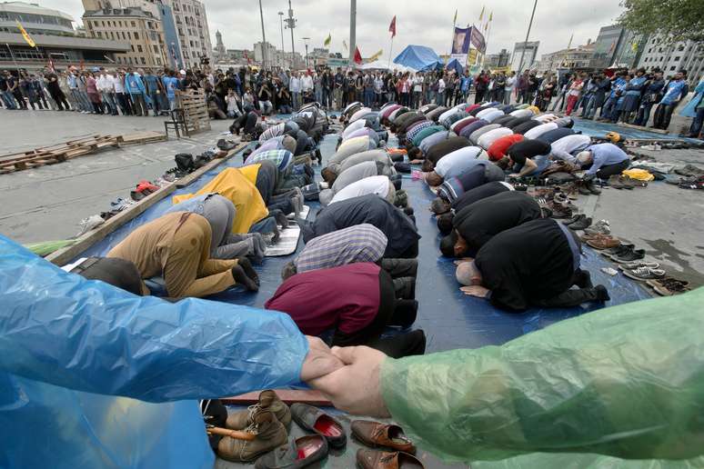 Manifestantes dão as mãos para proteger outros que rezam na Praça Taksim, em Istambul, nesta sexta-feira