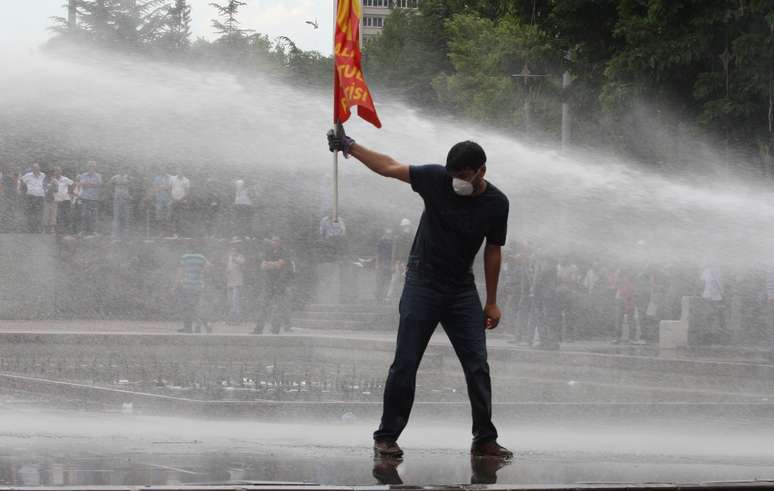 16 de junho - Manifestante segura bandeira enquanto policiais usam jatos de água para dispersar manifestação em Ancara