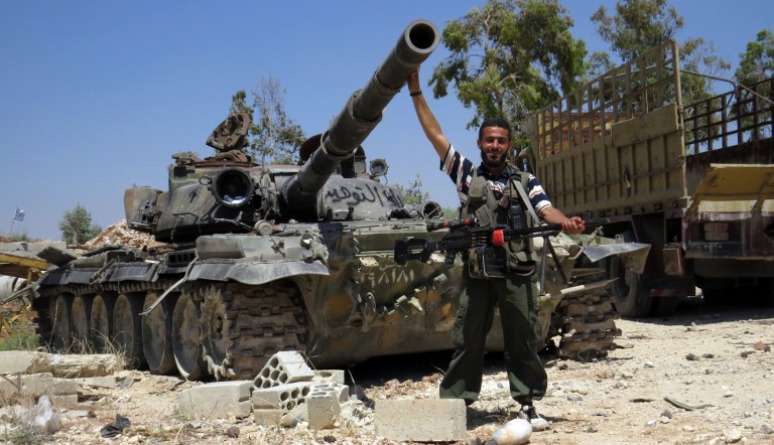 Soldado rebelde posa para a foto junto a um tanque, na cidade de Sermin