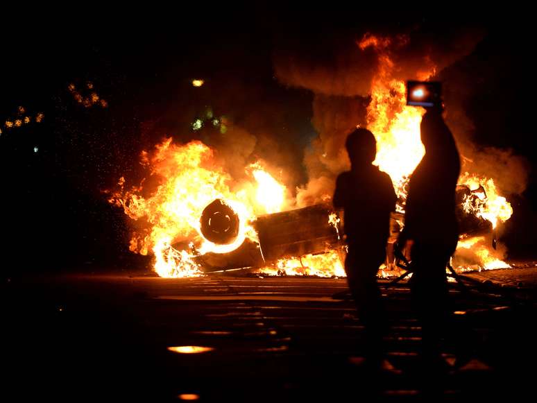 Jovens são vistos em frente ao carro queimado na noite de segunda-feira