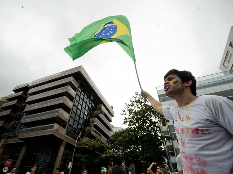 <p>Com bandeira do Brasil, manifestante faz coro a protesto na frente da casa de Cabral</p>