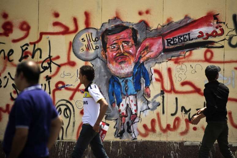 Manifestantes egípcios passam em frente a uma caricatura de Mursi pintada em uma parede do palácio presidencial, no Cairo