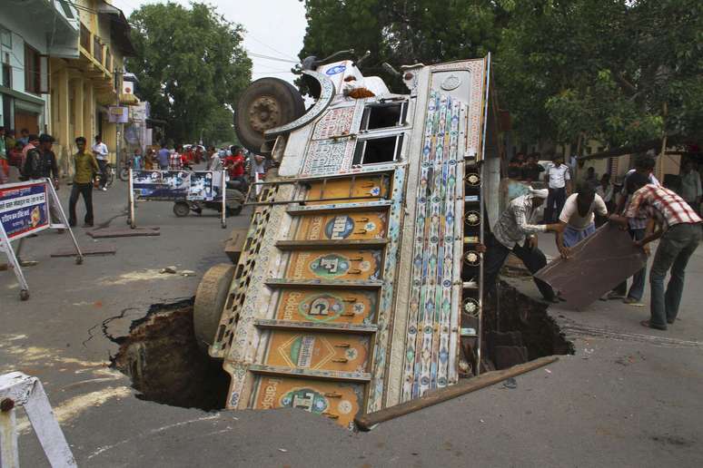 Um caminhão trefagava nesta rua em Ajmer, na Índia, quando um buraco se abriu e engoliu o veículo. A foto mostra a rua já isolada e com trabalhadores tentando salvar pertences que estavam sendo transportados.