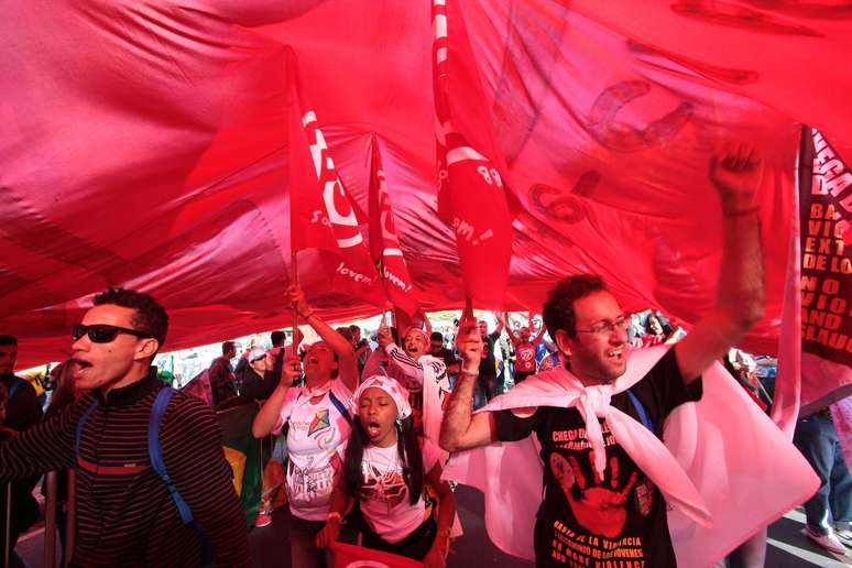 <p>Sob bandeira gigante, jovens protestam contra os gastos públicos da JMJ em meio à encenação da Via Crucis em Copacabana</p>