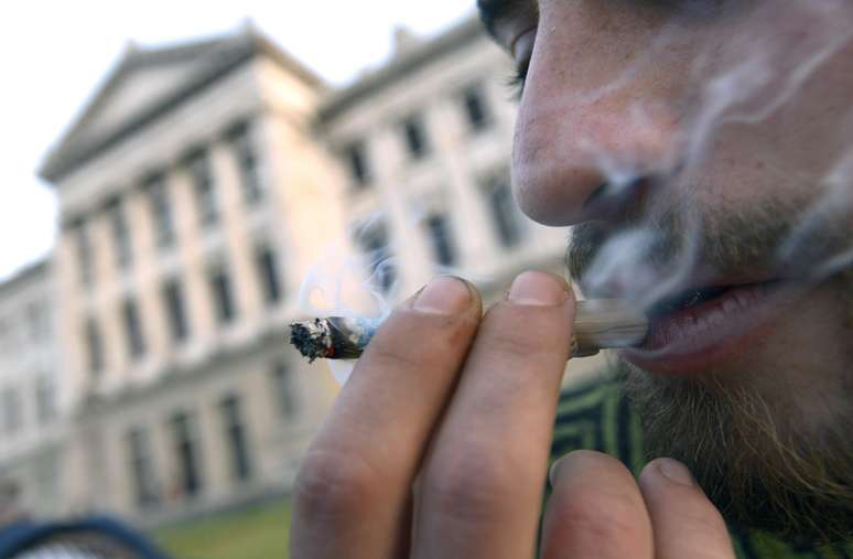 <p>Homem fuma maconha do lado de fora do Congresso uruguaio, onde o projeto foi votado na última quarta-feira</p>