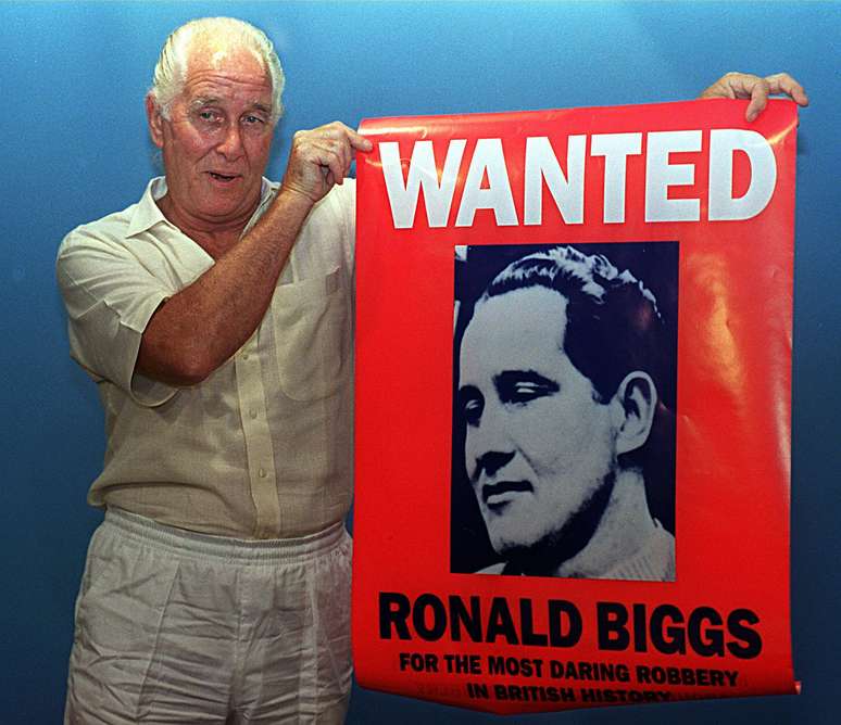 Ronald Biggs ao lado de seu cartaz de procurado no Rio de Janeiro em foto de 1994