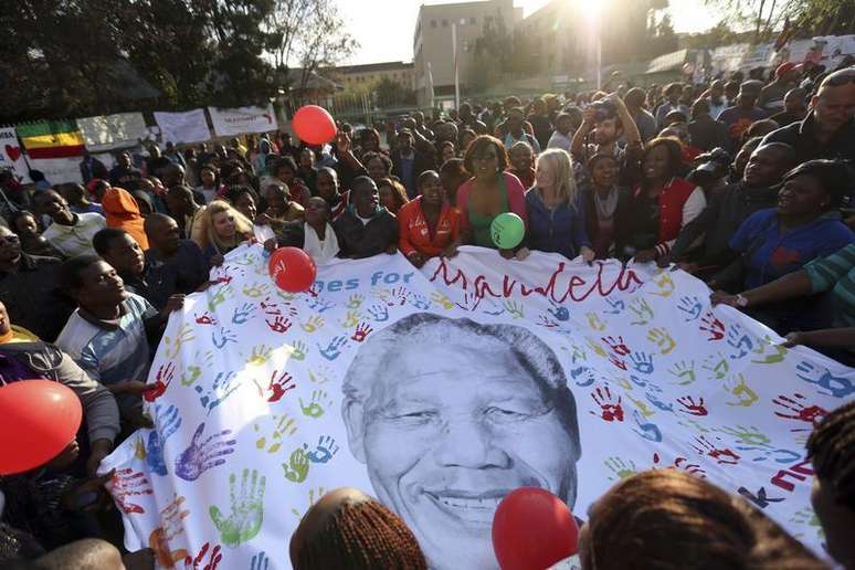 <p>Pessoas abrem um cartaz com a imagem de Nelson Mandela durante as comemora&ccedil;&otilde;es pelo seu 95&ordm; anivers&aacute;rio, em frente &agrave; cl&iacute;nica onde o ex-presidente da &Aacute;frica do Sul est&aacute; internado, em Pret&oacute;ria</p>