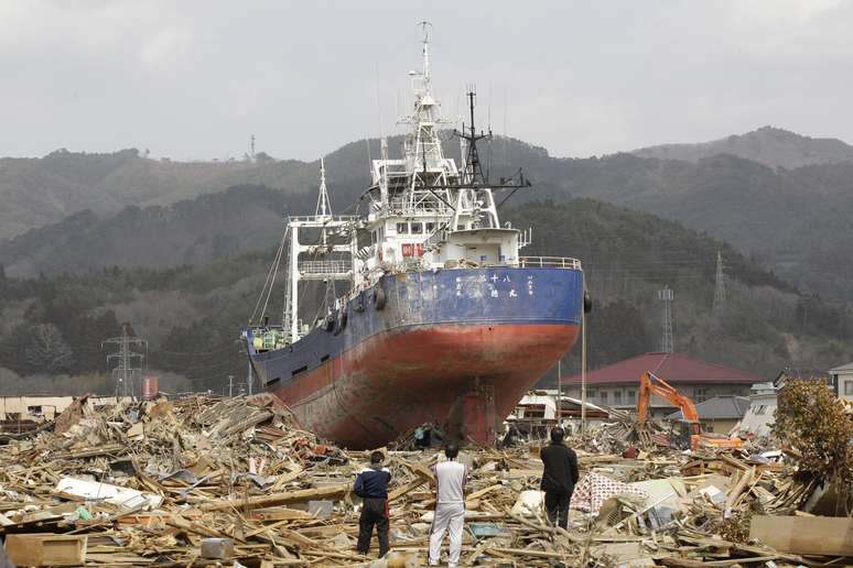 <p>Imagem do dia 2 de abril de 2011 mostra sobreviventes observando o navio pesqueiro encalhado em Kesennuma. A&nbsp;embarca&ccedil;&atilde;o&nbsp;estava no porto de Kesennuma - cidade de 70 mil habitantes no nordeste do Jap&atilde;o - quando foi arrastada 700 metros para dentro da cidade no dia 11 de mar&ccedil;o de 2011. A imagem ins&oacute;lita de um grande navio em meio a casas destru&iacute;das percorreu o mundo e se tornou um dos s&iacute;mbolos da trag&eacute;dia que se seguiu ao terremoto de 9 graus de magnitude, que custou cerca de 19 mil vidas. No fim de julho, moradores decidiram em um referendo que a embarca&ccedil;&atilde;o deve ser destru&iacute;da</p>