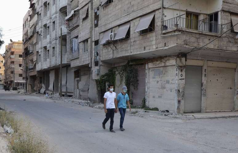 Homens usam máscara para se proteger de possíveis gases químicos ao se aventurarem por rua da área de Ain Tarma