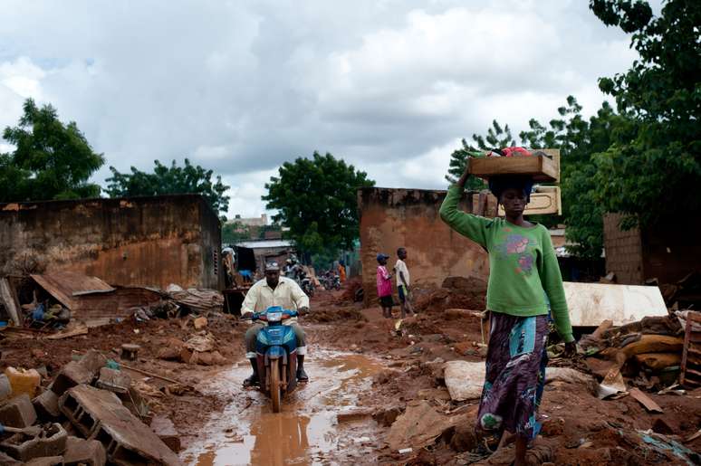Mulher carrega seus pertences após sua casa ser invadida por enchente, em Bamaco