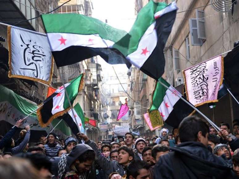 <p>Rebeldes marcham em Aleppo, cidade-berço da revolta síria, com a bandeira da Síria usada antes de Assad e adotada pela oposição ao regime</p>