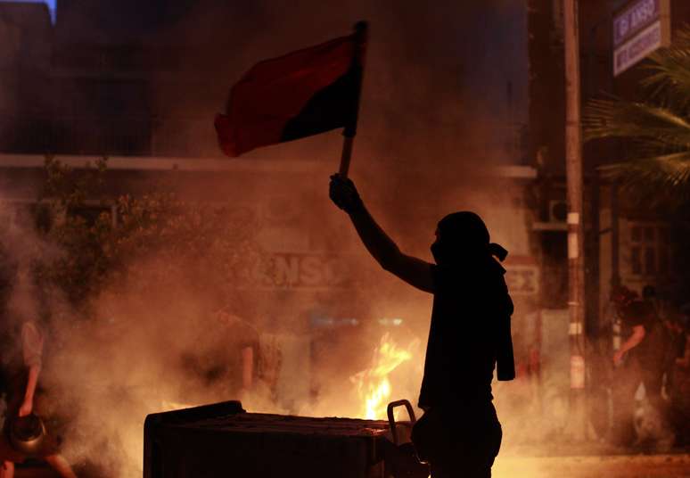 Manifestante exibe bandeira em frente &agrave; barricada durante protesto em Atenas