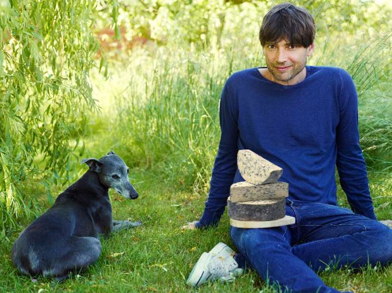 Alex James posa com queijo em sua fazenda, uma produtora artesanal