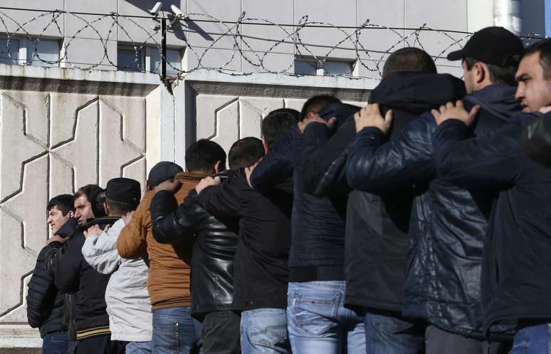 Trabalhadores detidos pela pol&iacute;cia formam fila para serem revistados no centro comercial palco de protestos e viol&ecirc;ncia na periferia de Moscou